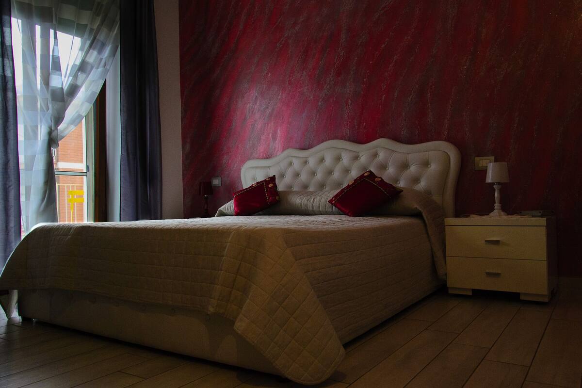 Een slaapkamer met een groot bed, een nachtkastje en een raam met gordijnen.
