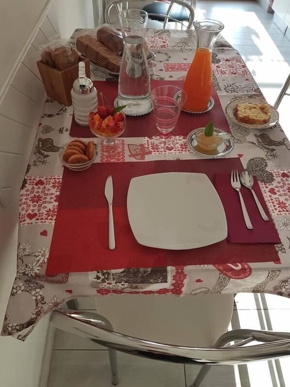 A dining table set with a red placemat, white plates, cutlery, and various food items including bread, fruit, and a pitcher of water. - B&B Domus Pompeii (Pompei)