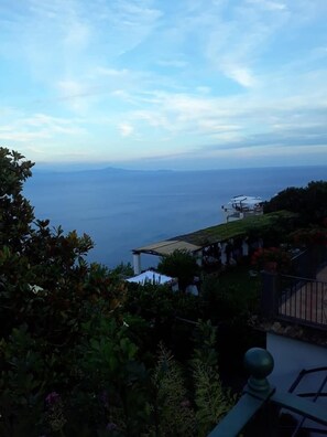 A coastal view with a clear sky, a distant horizon, and a building with outdoor seating.
