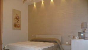 Een slaapkamer met een bed, nachtkastje, lamp en een schilderij aan de muur.