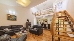 A spacious living area with a black leather sofa set, a wooden staircase, and a kitchen in the background. - Holiday home with pool and garden (Vodnjan)