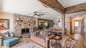 A spacious living room with a stone fireplace, a sofa, a coffee table, and a dining area with a kitchen in the background.