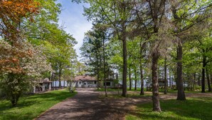 A pathway leading to a cabin with a lake view, surrounded by trees and grass.