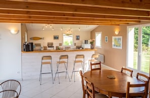 A kitchen with a wooden ceiling, a dining area with a round table and chairs, and a view of greenery outside. - Homerez - House in Sauzon (Sauzon)