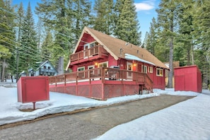 Eine zweistöckige Holzhütte mit roter Fassade, einem Balkon und verschneitem Gelände.