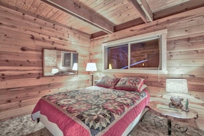 Ein Schlafzimmer einer Holzhütte mit einem Bett, einem Fenster und einem kleinen Tisch mit einer Lampe.