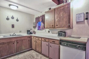 Una cocina con gabinetes de madera, lavavajillas, microondas y una ventana con cortinas.