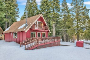 Una cabaña roja con balcón y escaleras que conducen a la entrada, rodeada de nieve y árboles.