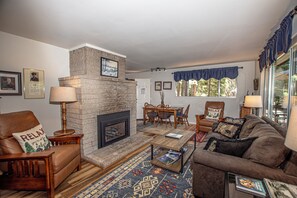 Una sala de estar con chimenea, muebles de cuero, un comedor y un ventanal con cortinas.