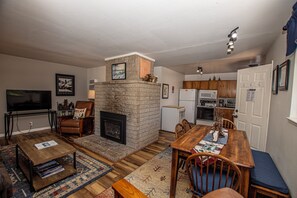 A living room with a fireplace, a television, a dining table, and a kitchen area.
