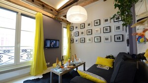 A living room with a sofa, a table with food, a TV, and framed pictures on the wall. - D4DG Watergate (Paris)
