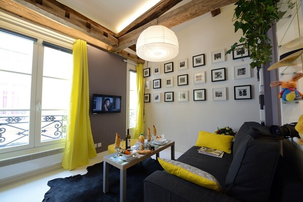 Un salon avec un canapé, une table garnie de nourriture, un téléviseur et des tableaux encadrés accrochés au mur.