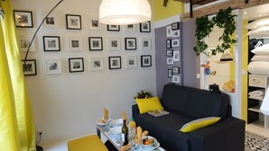 A modern living room with a dark sofa, yellow cushions, a dining table with breakfast items, and a wall adorned with framed pictures. - D4DG Watergate (Paris)