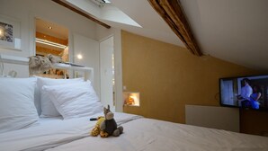 A hotel room with a bed, a television, a stuffed toy, and a small shelf with items.