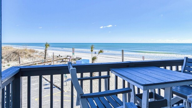 A beach view from a covered deck with wooden benches and tables. - Sea Master 105 - Two Bedroom, Two Bath Oceanview Condo (Murrells Inlet)