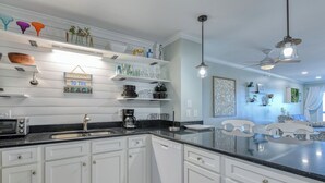 A modern kitchen with white cabinetry, a black countertop, and a dining area with a white table and chairs. - Sea Master 105 - Two Bedroom, Two Bath Oceanview Condo (Murrells Inlet)