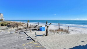 A beachside parking area with a clear view of the ocean, a wooden walkway leading to the beach, and a blue trash bin. - Sea Master 105 - Two Bedroom, Two Bath Oceanview Condo (Murrells Inlet)