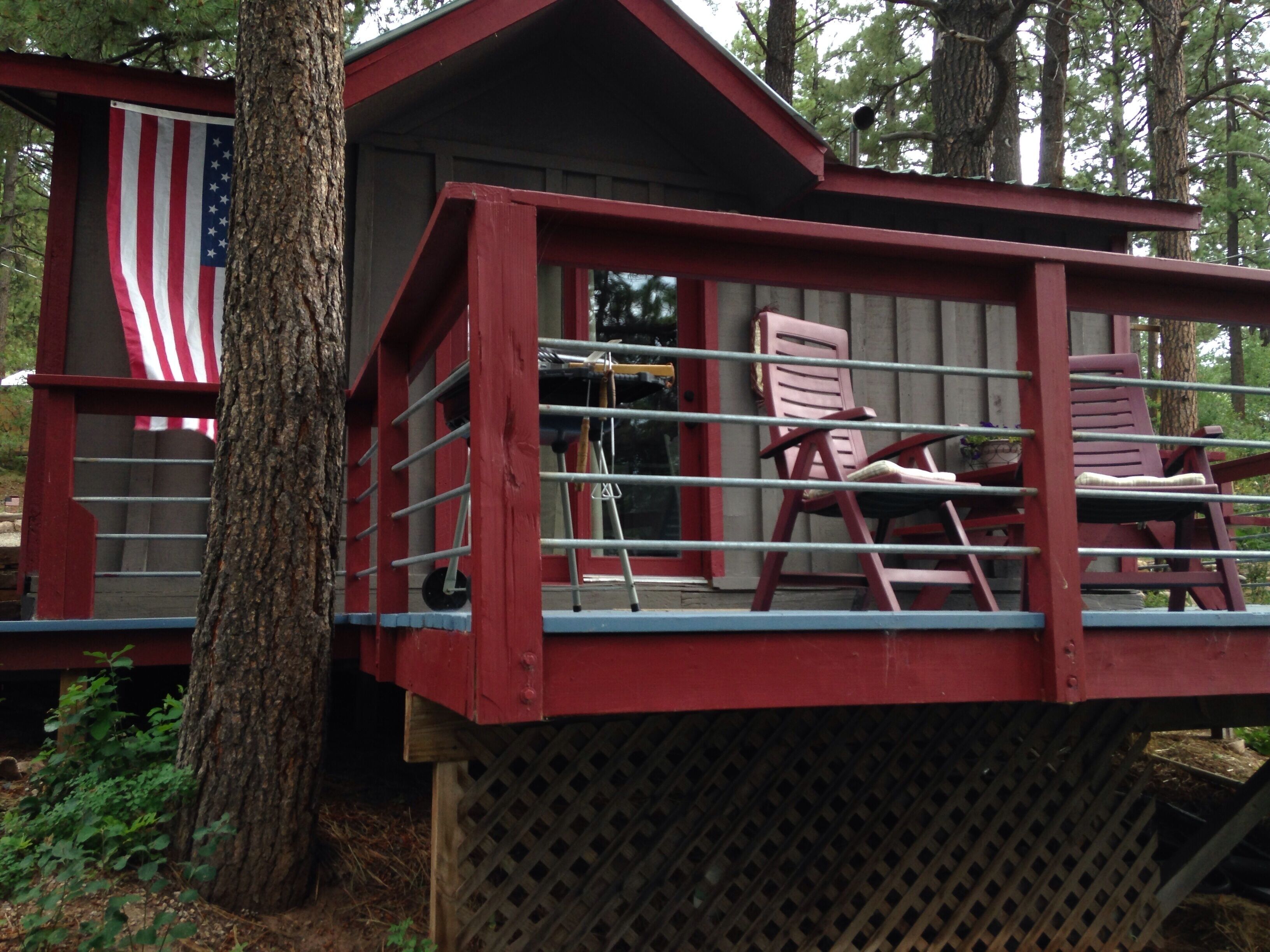 A rustic cabin with a red exterior, a wooden deck, and two Adirondack chairs.