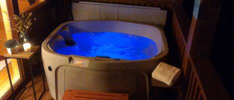 A hot tub with a wooden deck and a small table with a candle.