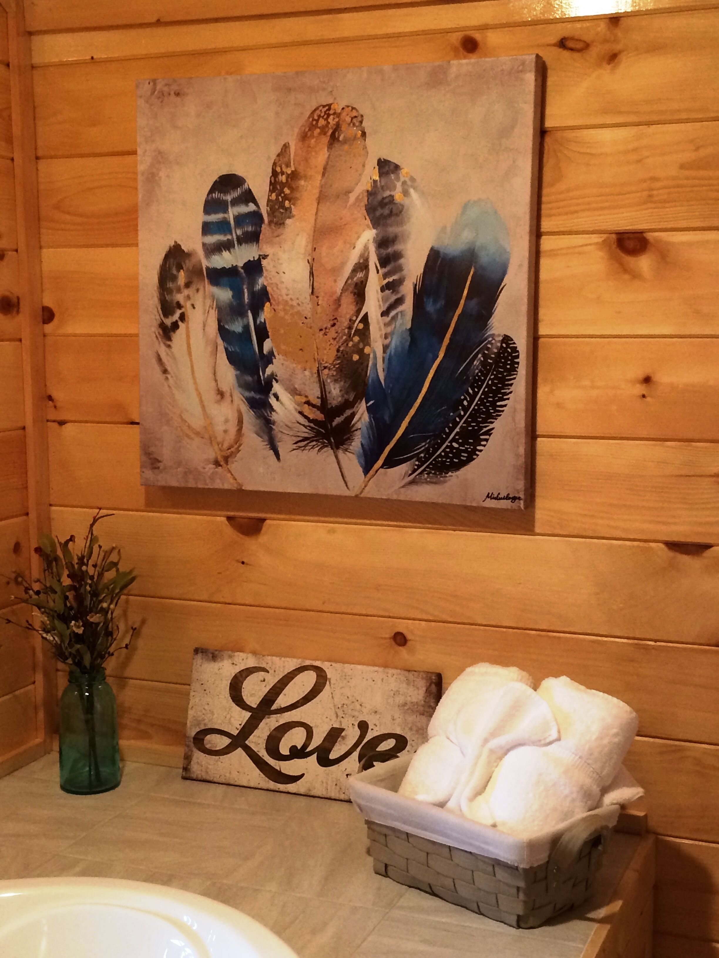 A wooden cabin interior with a painting of feathers, a sign reading "Love", and a basket of towels.