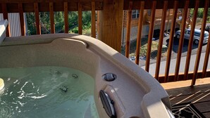 Un jacuzzi en una terraza de madera con vistas a montañas y una casa al fondo.