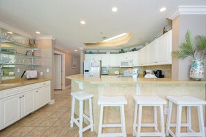 Una cocina moderna con armarios blancos, una isla central con taburetes, un microondas y un refrigerador.