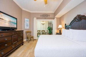 Habitación de hotel con cama, televisor, cómoda de madera, escritorio y sillas, y vista a la playa.