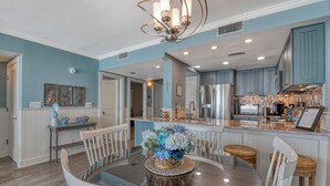A modern kitchen with a central island, a dining area with a glass table, and a living space with a chandelier. - One Ocean Place 1102 2 Bedrooms, 2 Bathrooms, Oceanfront (Garden City Beach)