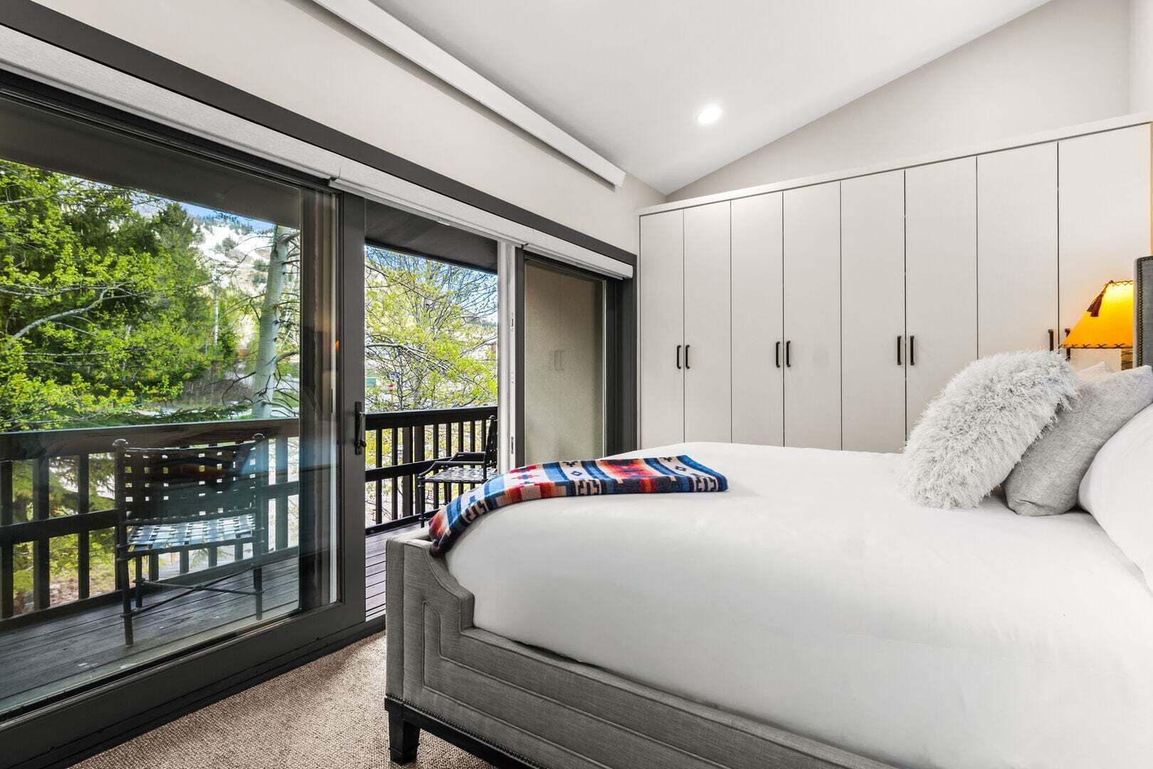 A bedroom with a large bed, a balcony with a table and chairs, and a wardrobe.