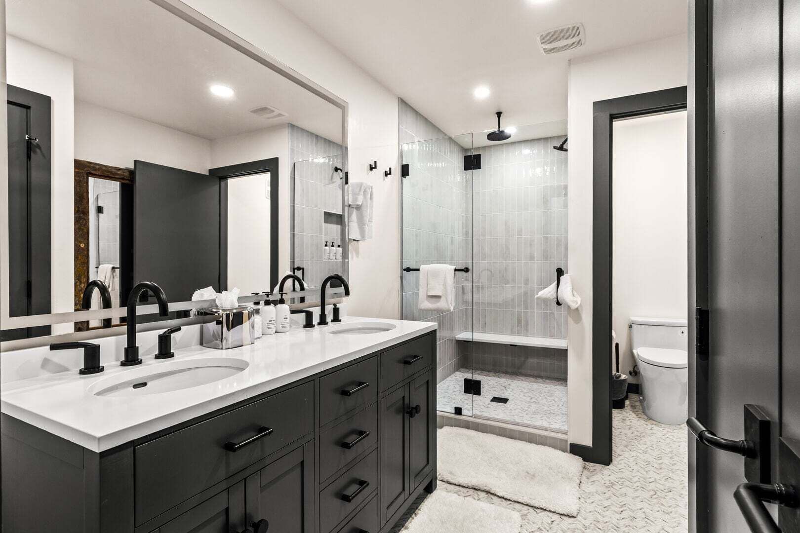 A modern bathroom with dual sinks, a large mirror, and a walk-in shower.