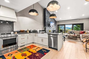 Een moderne keuken met een centraal eiland, roestvrijstalen apparatuur en hangende lampen.
