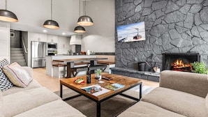 A modern living room with a fireplace, a kitchen with stainless steel appliances, and a stone accent wall. - RMR: Four Seasons I Unit 6 Condo in Teton Village (Teton Village)
