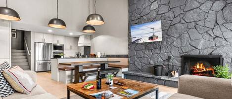 A modern living room with a fireplace, a kitchen with stainless steel appliances, and a stone accent wall.