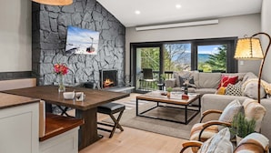 A modern living room with a stone wall, fireplace, dining area, and large windows offering a view. - RMR: Four Seasons I Unit 6 Condo in Teton Village (Teton Village)