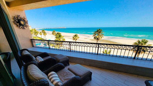 A balcony with wicker furniture overlooking a beach.