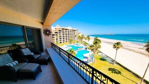 A balcony with a view of a beach, a pool, and a hotel building.