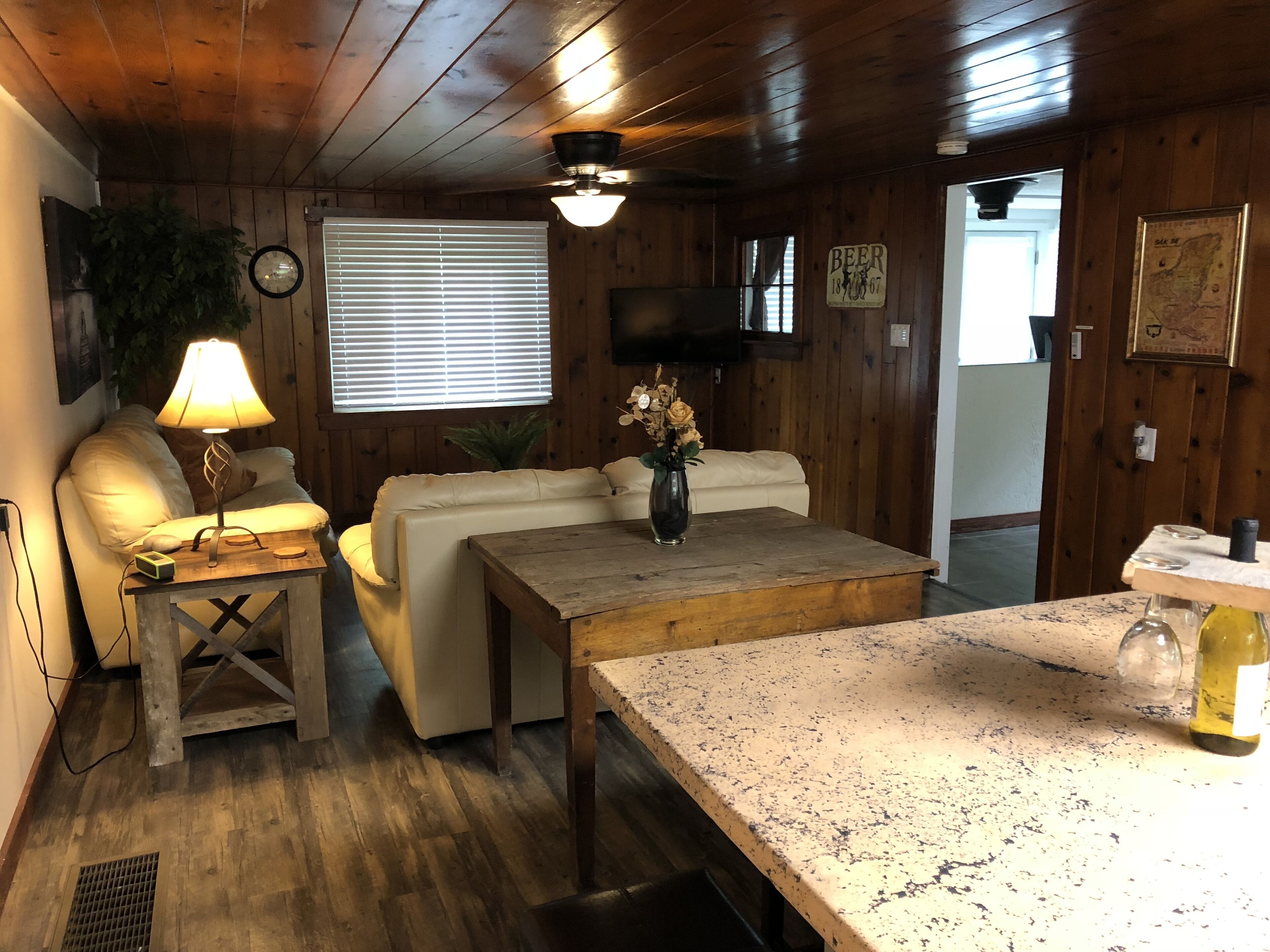 L’intérieur d’un chalet accueillant, avec un plafond en bois, un canapé blanc, une table basse en bois et une petite table avec une lampe.