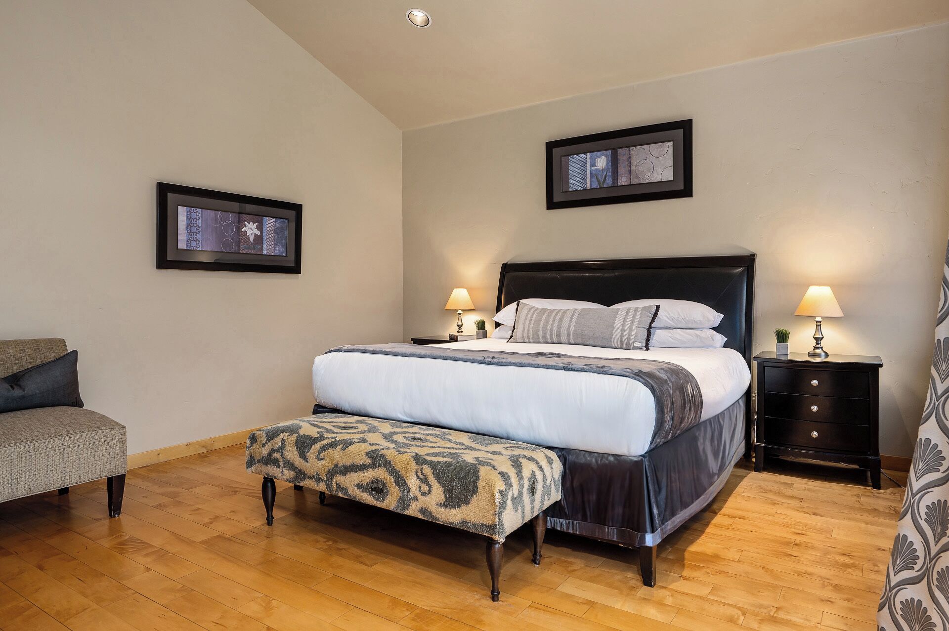 Una camera da letto ben ordinata con un letto grande, due comodini, una panca e due quadri appesi alle pareti.
