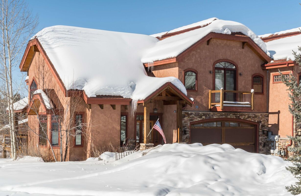 A large, two-story house with a snow-covered roof and a stone foundation.