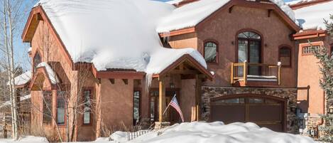 A large, two-story house with a snow-covered roof and a stone foundation.