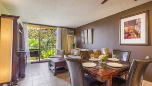 A dining area with a table set for four, a sofa, and a view of greenery through large windows.