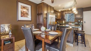 A dining area with a wooden table set for four, surrounded by chairs. A ceiling fan and pendant lights are visible above.