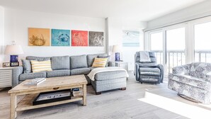 Een moderne woonkamer met een grijze bank, een poef en een gestreept fauteuil. Boven de bank hangen vier kunstwerken aan de muur.