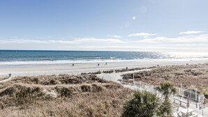 Een strand met een zandpad dat leidt naar een witte omheining en palmbomen.