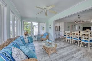 Ein großzügiger Wohnbereich mit einer großen Couch, Korbstühlen, einem Glastisch und einem Esstisch mit Stühlen.