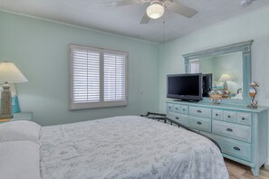 A bedroom with a bed, a dresser, a television, and a ceiling fan.