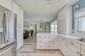 A kitchen with white cabinets, a stainless steel refrigerator, and a dining area with a table and chairs.