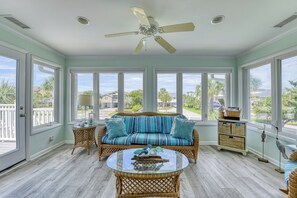 A sunroom with a wicker sofa, a glass coffee table, and a ceiling fan.