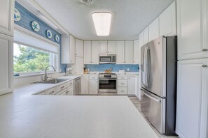 A kitchen with white cabinets, a stainless steel refrigerator, a microwave, and a window with a view of greenery.