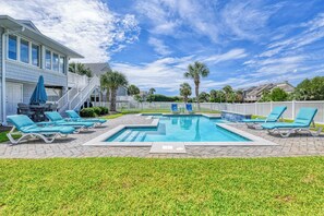 A swimming pool with lounge chairs, a covered patio area, and a white fence.